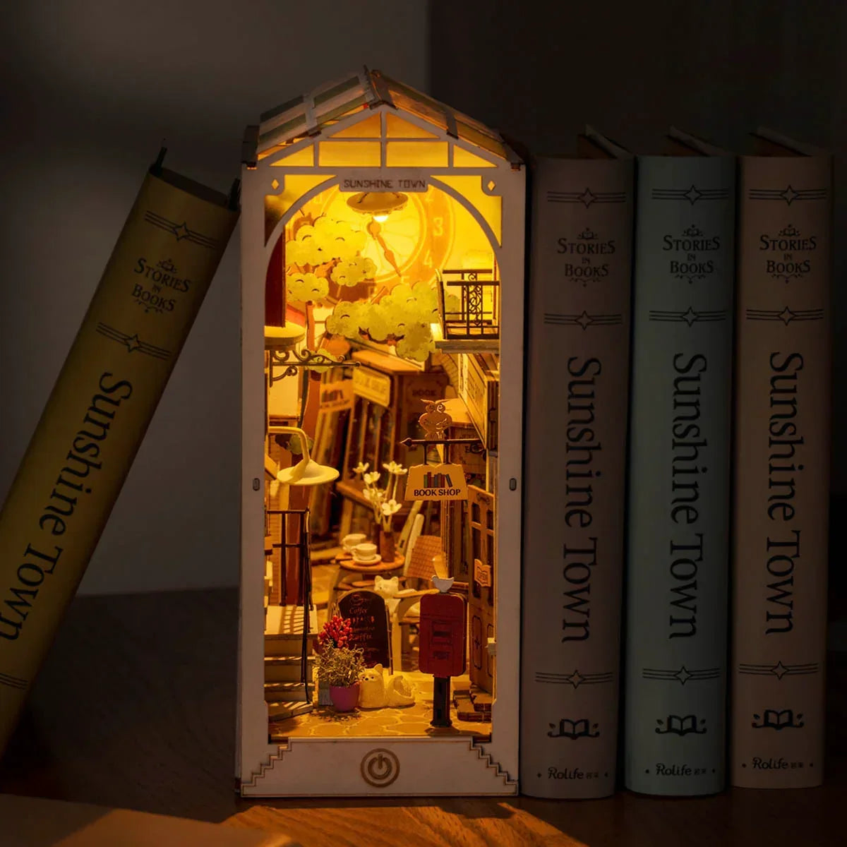 Beleuchtetes Buchstützenmodell einer Miniatur Buchhandlung zwischen echten Büchern im Regal