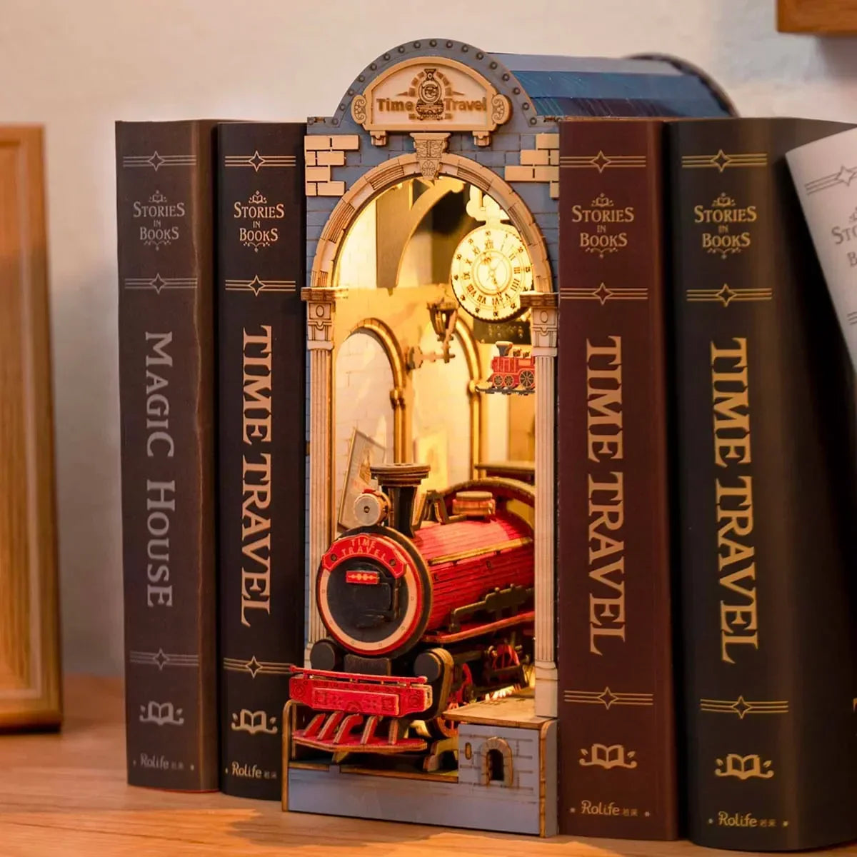 Buchstütze mit beleuchtetem Modell einer Dampflokomotive in einem Bahnhofsbogen zwischen Buchrücken