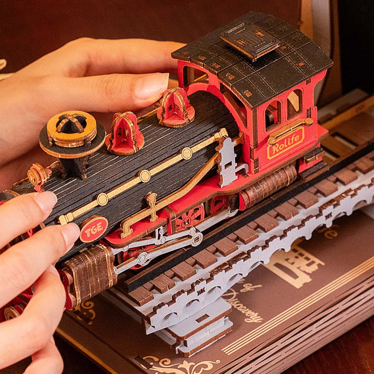 Hände halten ein rotes und schwarzes Holzmodell einer Dampflokomotive auf einem Gleis
