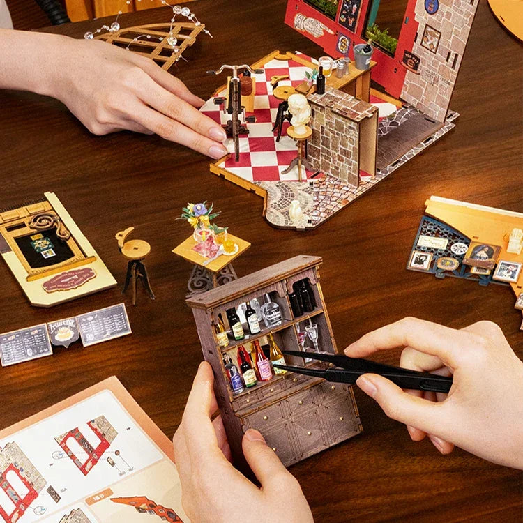 Hände bauen ein Miniatur-Puppenhaus mit winzigen Möbeln und Accessoires auf einem Holztisch