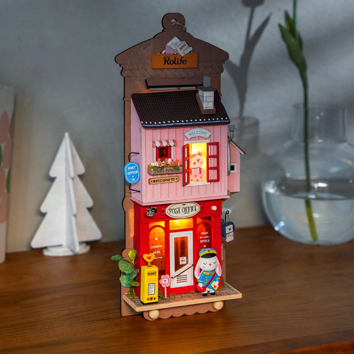 Miniatur Postamt aus Holz mit beleuchtetem Innenraum und einer Hasenfigur als Postbote