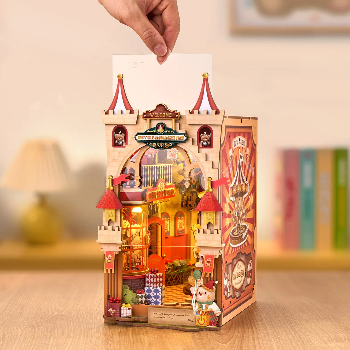 Eine Hand schiebt ein weißes Blatt Papier in ein Miniatur-Märchenschloss-Bücherregal mit Lichtern
