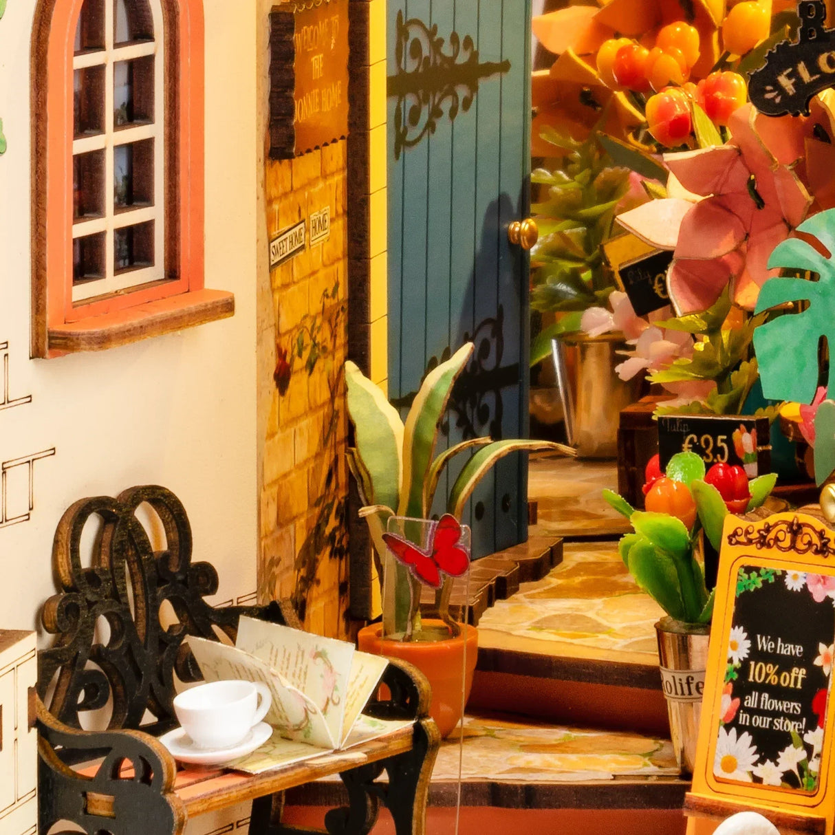 Miniatur Blumenladen mit Bank Tasse und aufgeschlagenem Buch vor einer blauen Tür