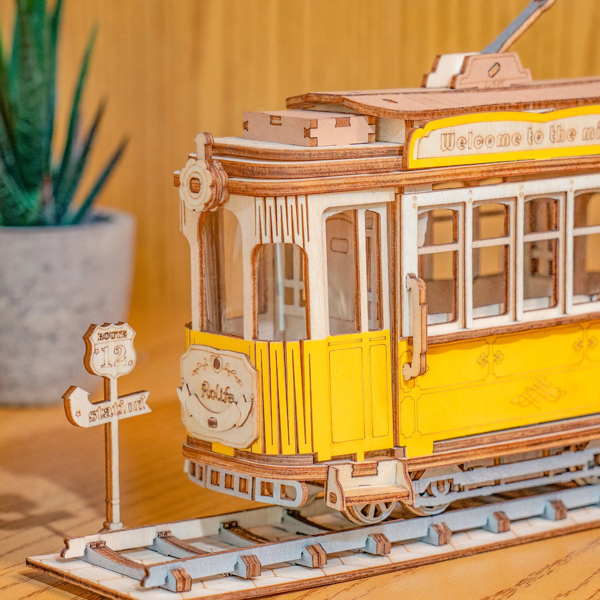 Holzmodell einer gelben Straßenbahn auf Schienen mit einem Haltestellenschild