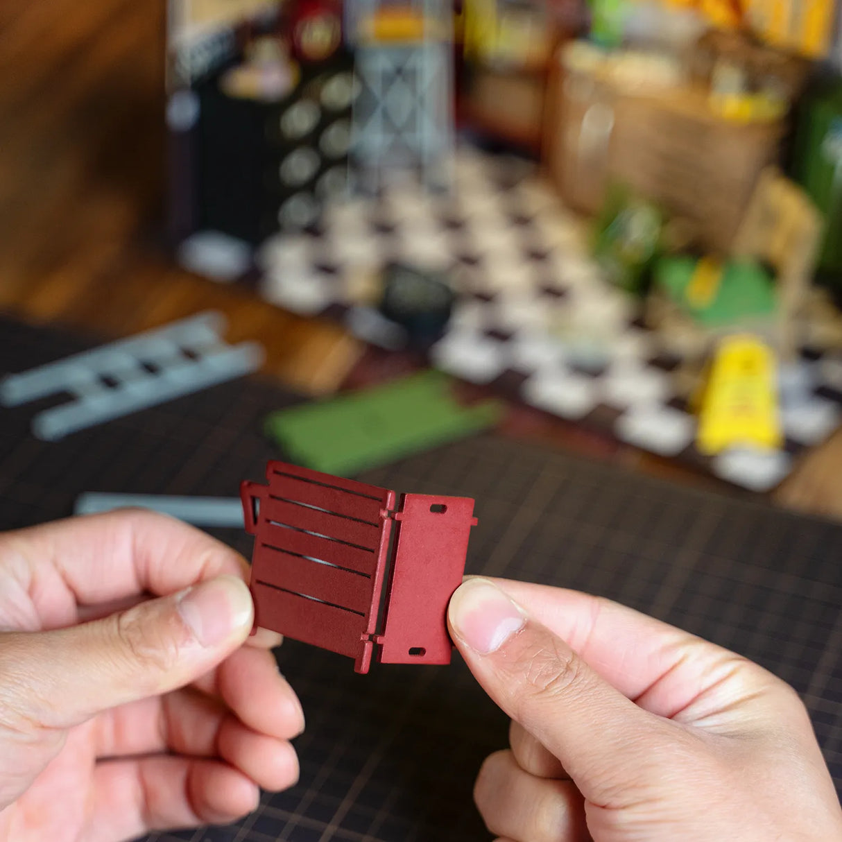 Hände halten ein kleines rotes Bauteil aus einem Modellbausatz