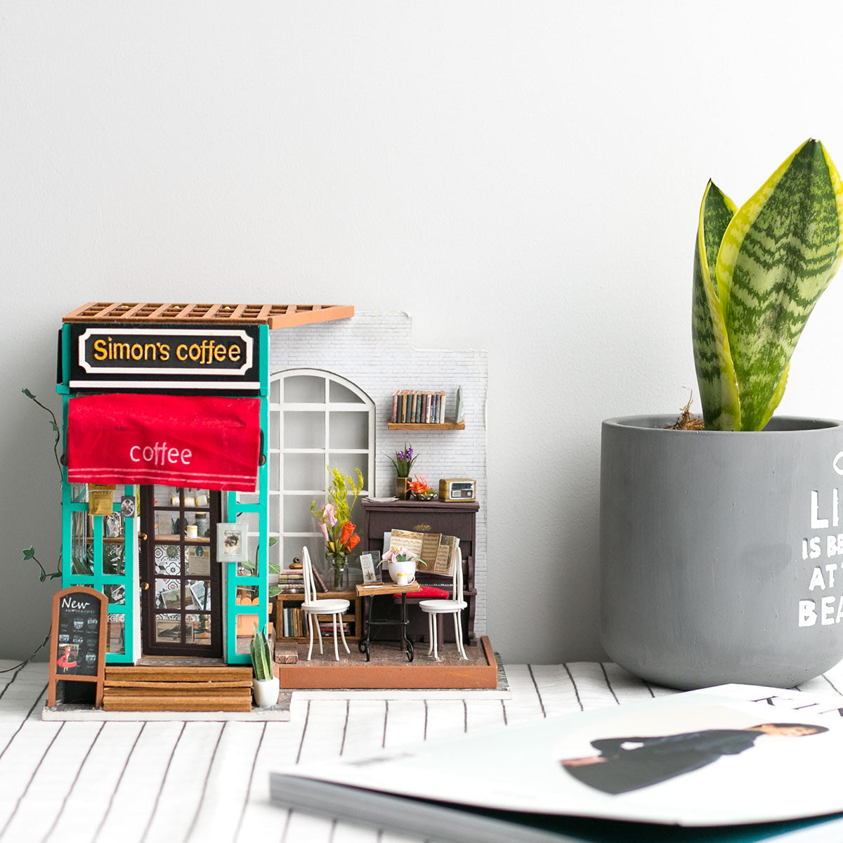 Miniaturmodell eines Cafes mit Tischen Stuehlen und einer Zimmerpflanze im grauen Topf daneben