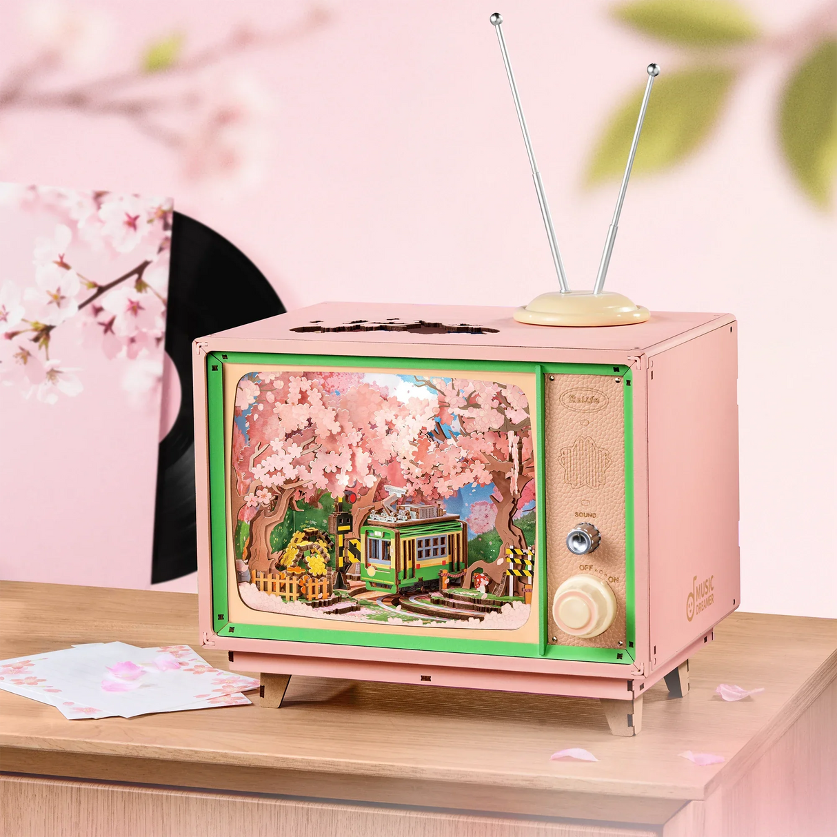 Rosa Miniatur-Fernseher mit Kirschblüten und Straßenbahn-Diorama auf Holztisch