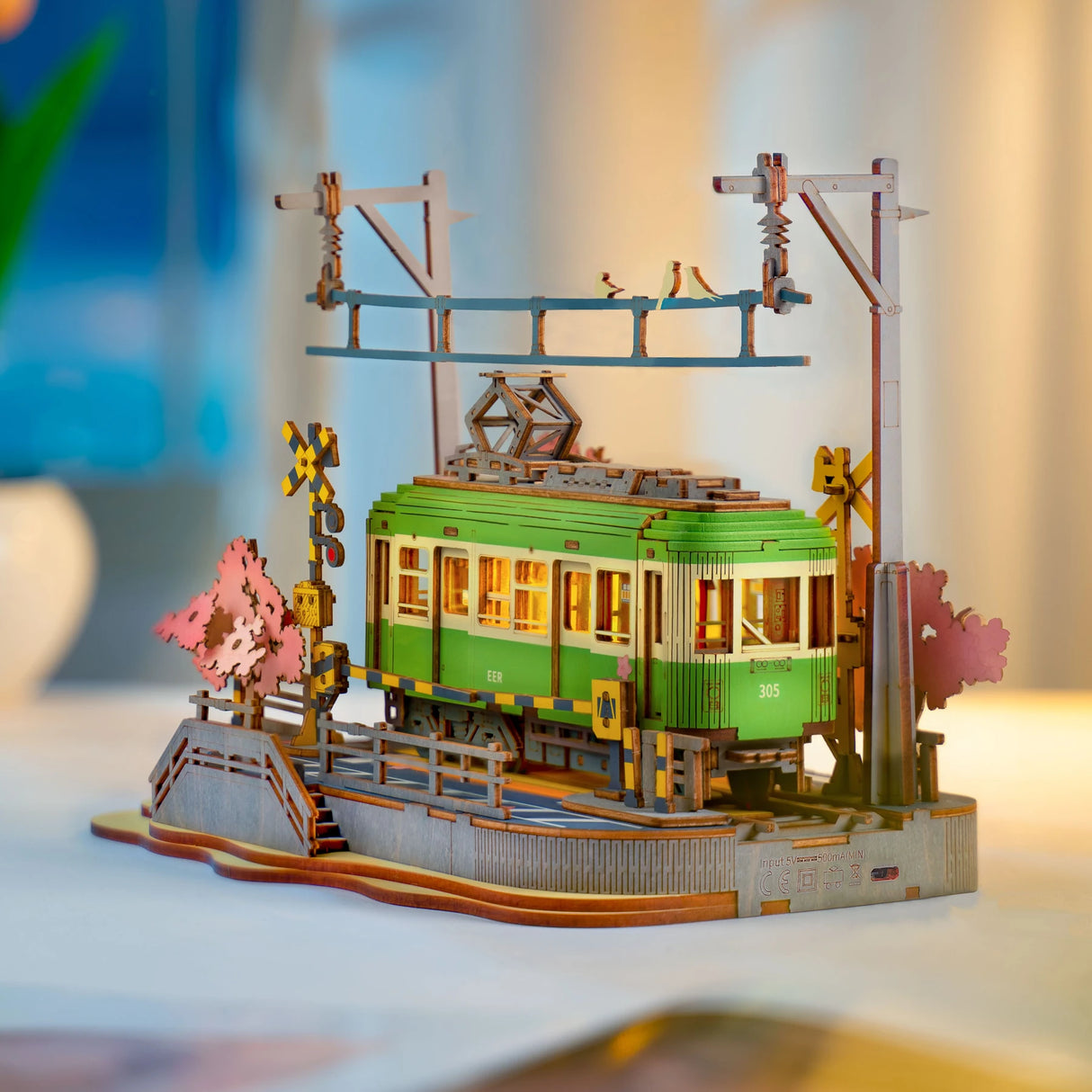 Modell einer grünen Straßenbahn aus Holz mit Oberleitung und Kirschblütenbäumen