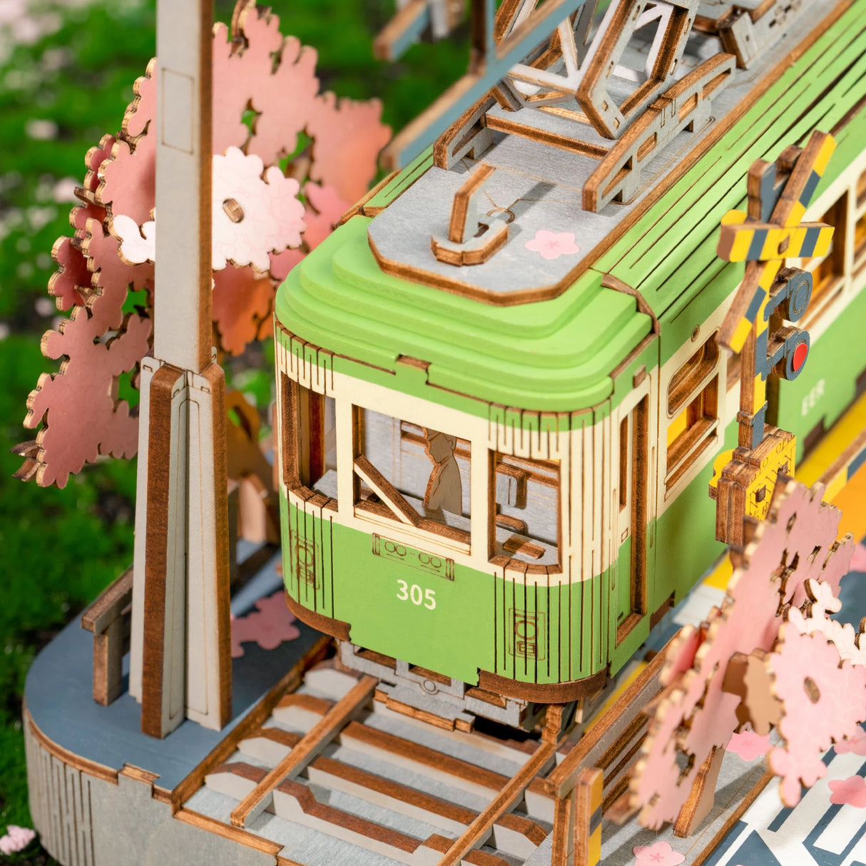 Holzmodell einer grünen Straßenbahn mit Kirschblütenbäumen an einem Bahnübergang