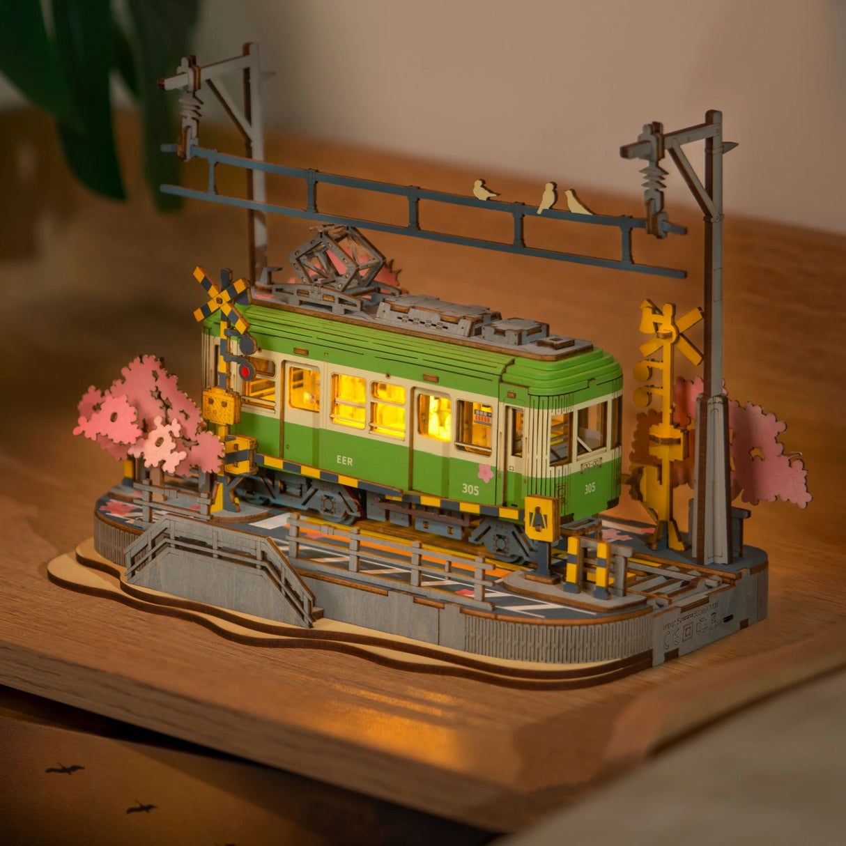 Beleuchtetes Holzmodell einer grünen Straßenbahn mit Kirschblütenbäumen und Bahnschranken