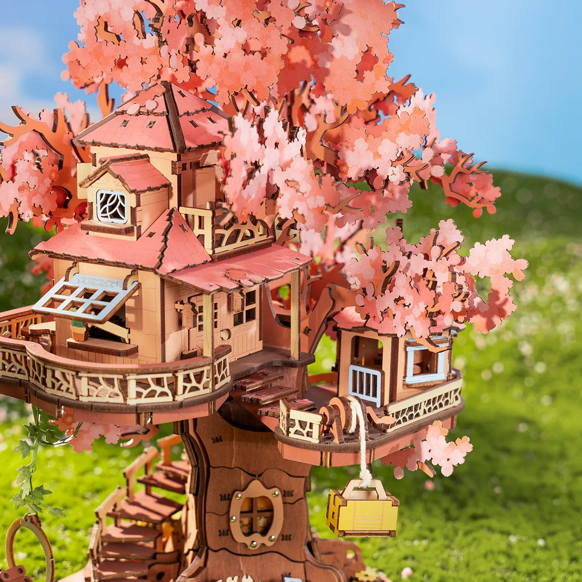 Baumhaus-Modell aus Holz mit rosa Blättern und grüner Wiese im Hintergrund