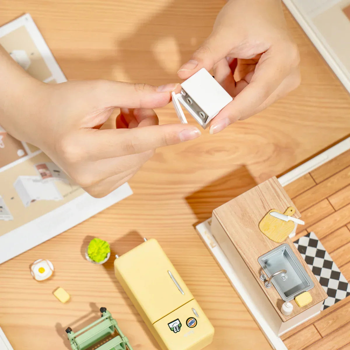 Hände beim Zusammenbau eines Miniatur Küchenschranks aus einem Bastelset