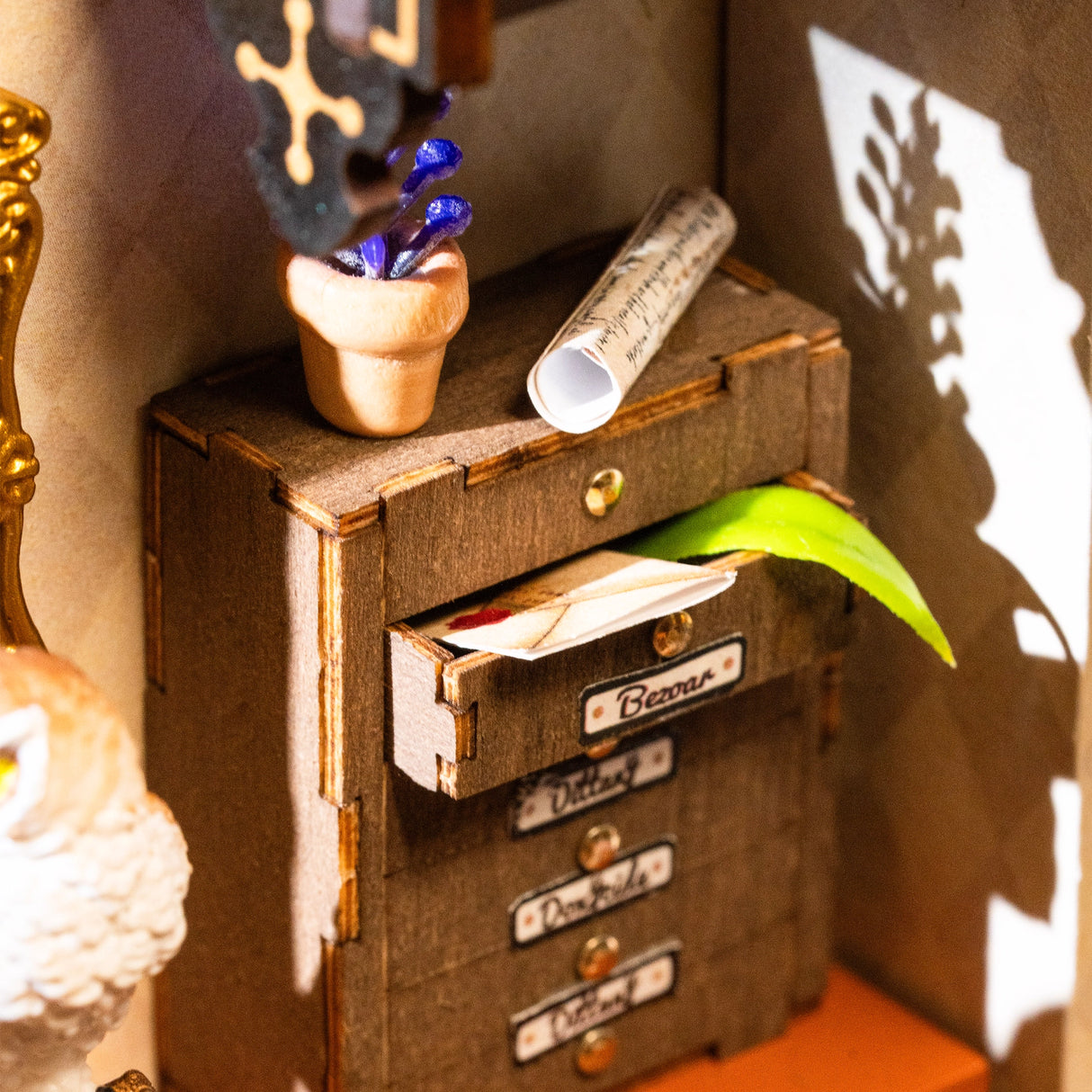 Nahaufnahme eines Miniatur-Schubladenschranks mit Briefen und einem grünen Blatt, daneben eine Pflanze und eine Schriftrolle