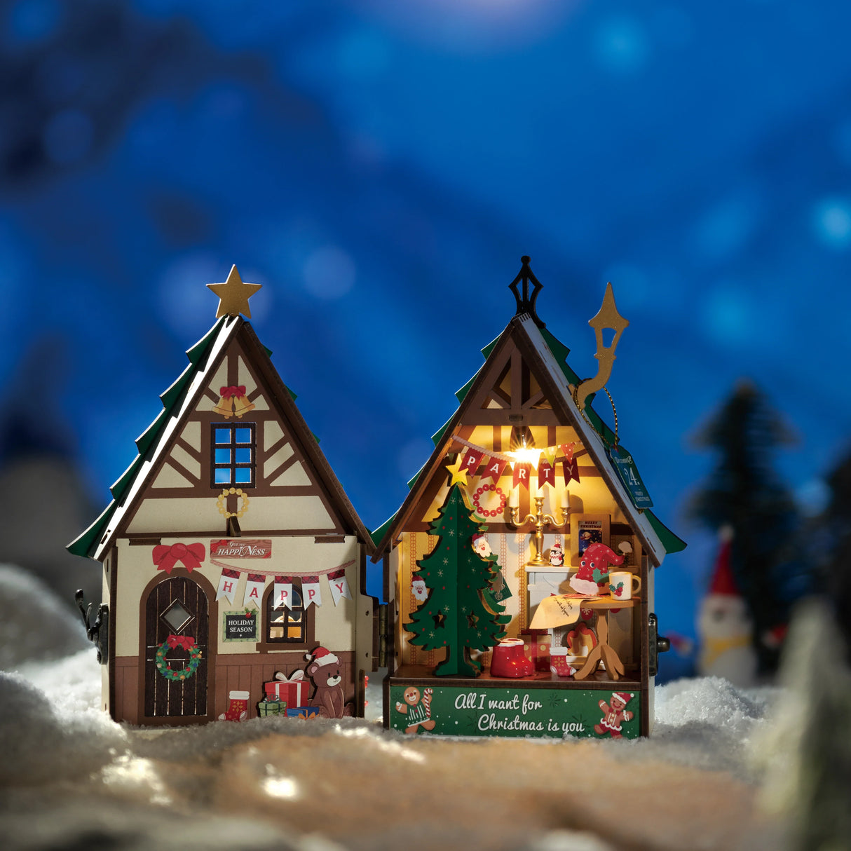 Zwei beleuchtete Weihnachtshäuser aus Holz im Schnee