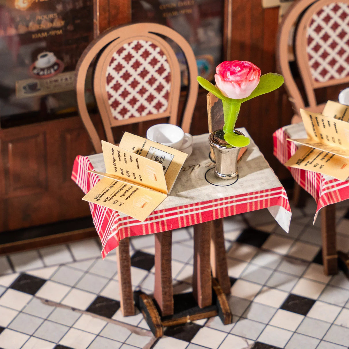 Miniatur-Café-Tisch mit rot-weiß karierter Tischdecke, Menü, Tasse und rosa Blume
