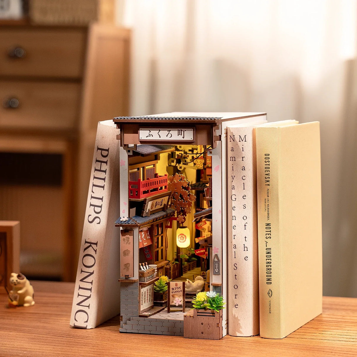 Miniatur-Buchstütze mit beleuchteter japanischer Gasse zwischen zwei Büchern auf einem Holztisch