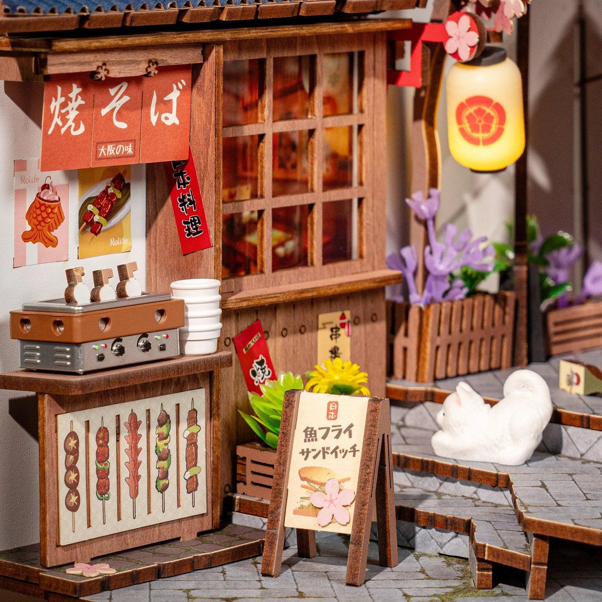 Miniatur-Straßenstand mit japanischen Schriftzeichen, Grill, Spießen und einem weißen Kätzchen