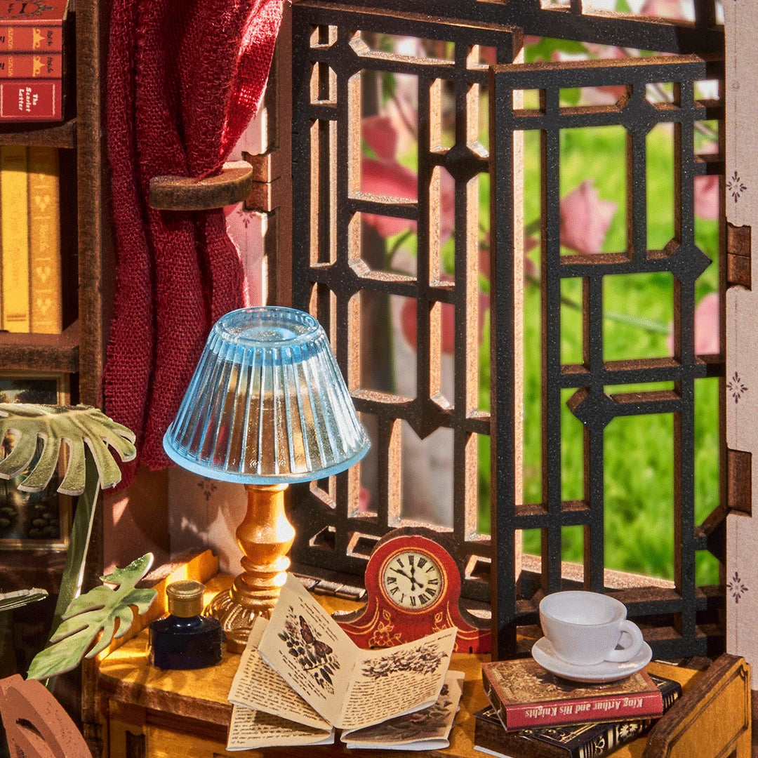 Miniaturmodell eines Zimmers mit Schreibtischlampe, aufgeschlagenem Buch, Uhr und Fenster mit Blick ins Grüne