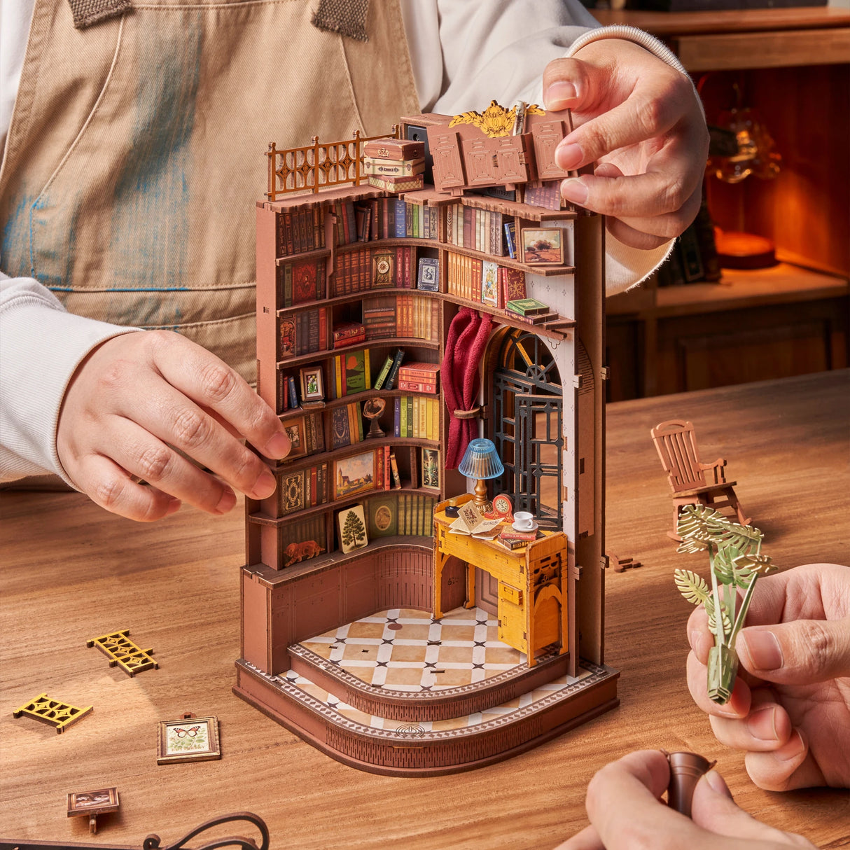 Person baut ein detailliertes Miniaturmodell einer Bibliothek aus Holzbauteilen zusammen