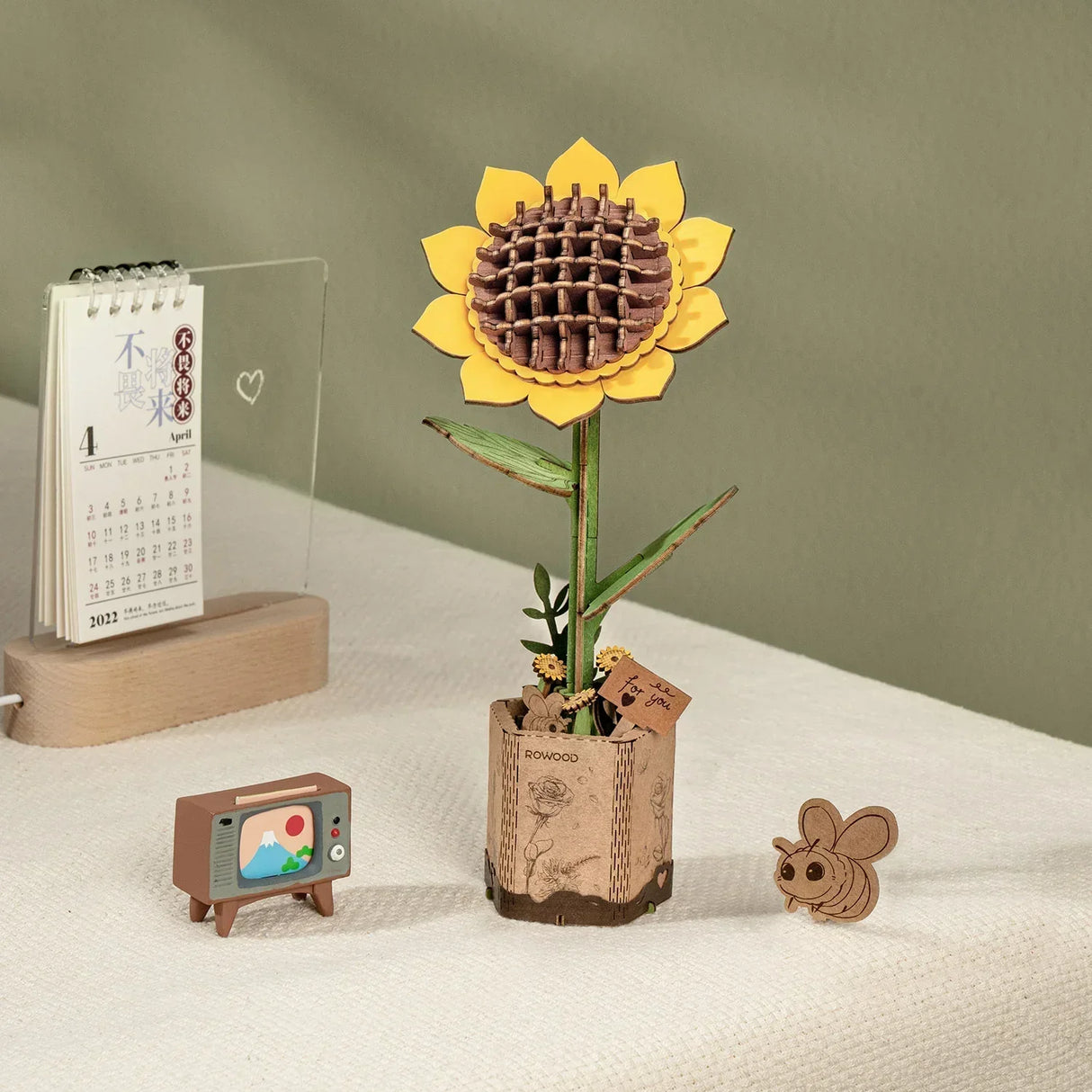 Holzbausatz einer Sonnenblume im Topf mit kleiner Fernsehfigur und Bienenfigur auf einem Tisch