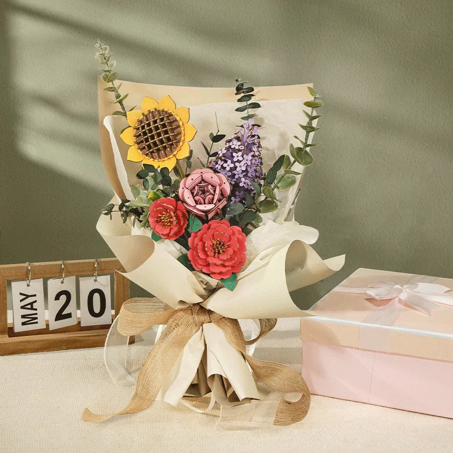 Ein Blumenstrauß aus Papier mit Sonnenblume und Rosen neben einem Kalender und einer Geschenkbox