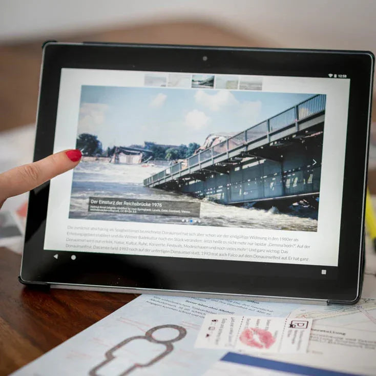 Finger zeigt auf ein Tablet mit einem historischen Foto vom Einsturz der Wiener Reichsbrücke