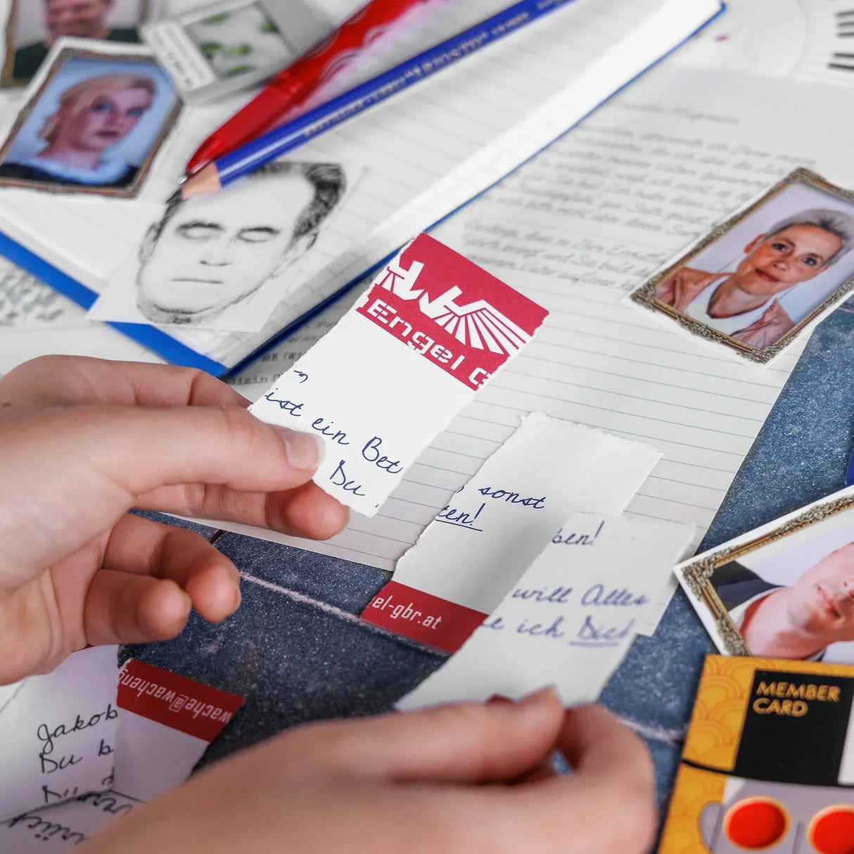 Hand haelt Zettel mit Notizen und Portraetfotos auf einem Schreibtisch
