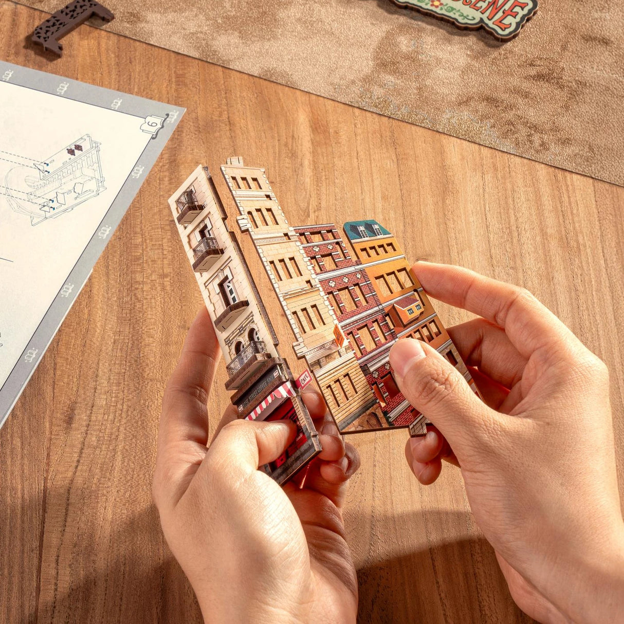Hände halten ein 3D-Puzzle eines Gebäudes mit Balkonen und einem Café
