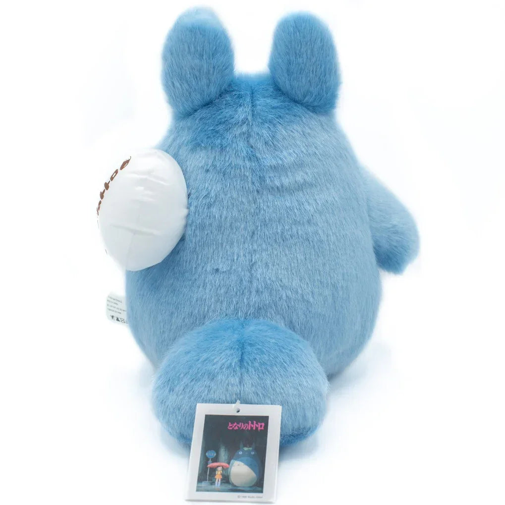 Rückansicht eines blauen Totoro Plüschtiers mit weißem Beutel und Produktetikett