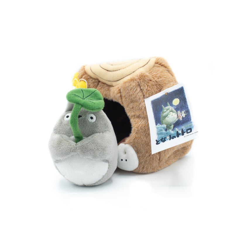 Plüschfigur von Totoro mit einem Blatt in der Hand vor einem Baumstumpf