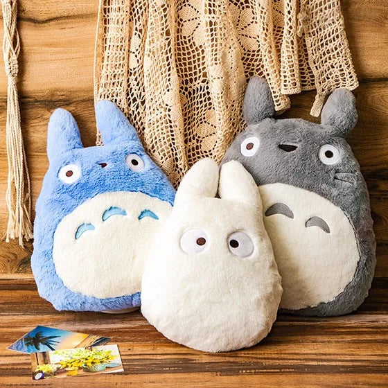 Drei Plueschfiguren in Form von Totoro in Blau Weiss und Grau vor einem beigen Makramee Wandbehang