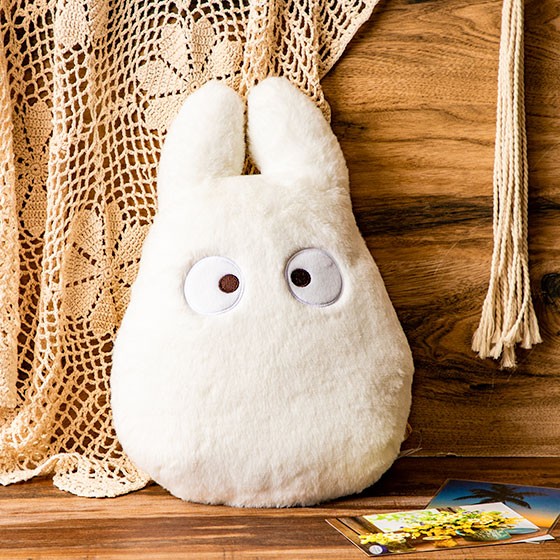 Weißes Plüschkissen in Form einer Totoro Figur vor einem gehäkelten Vorhang