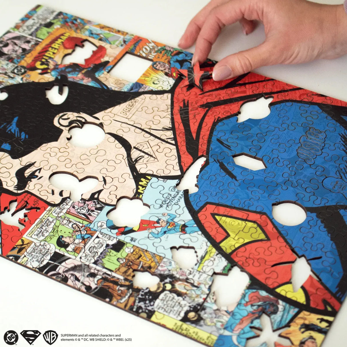 Eine Hand platziert ein Puzzleteil in einem Superman-Puzzle mit Comic-Motiven