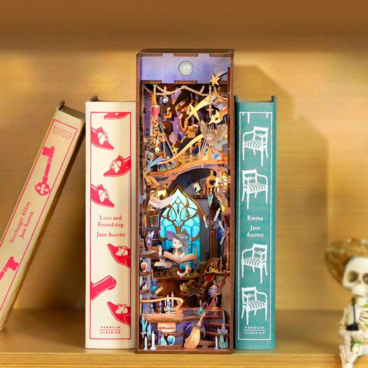 Ein Bücherregal-Einsatz mit einer Miniatur-Hexenwerkstatt, umgeben von drei Büchern