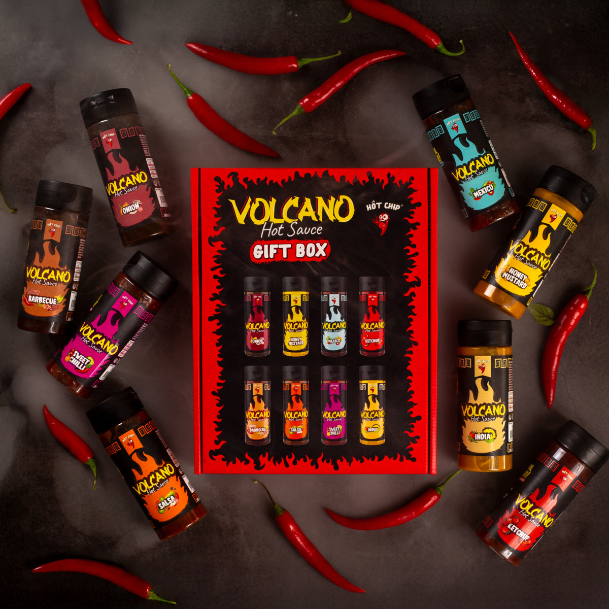 Geschenkbox mit 8 Volcano Hot Sauces, umgeben von einzelnen Flaschen und roten Chilischoten