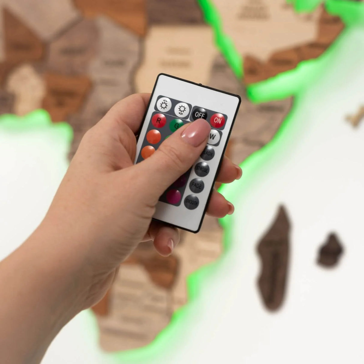 Hand hält eine Fernbedienung zur Steuerung der LED Beleuchtung einer Holzweltkarte