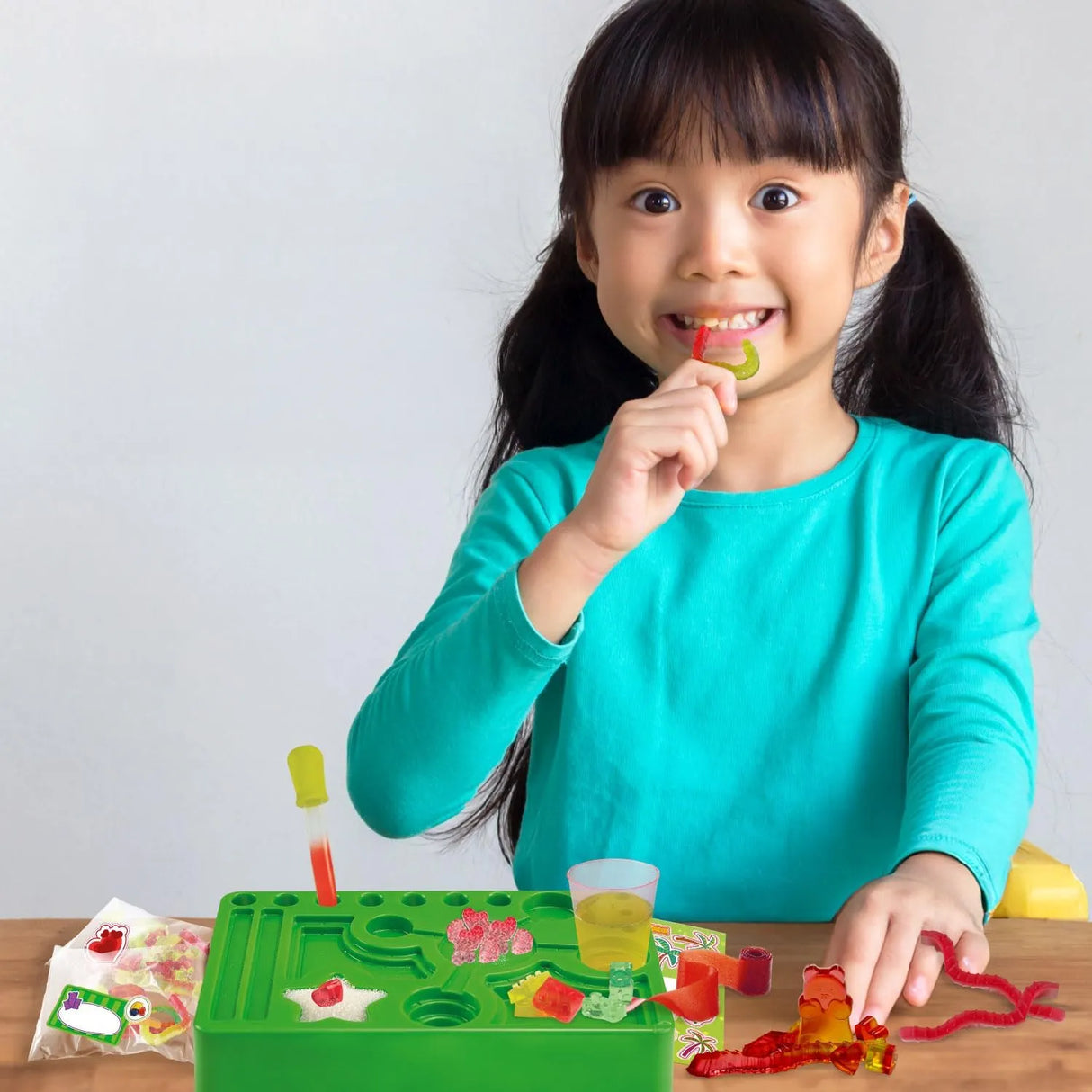 Mädchen mit Zöpfen isst einen roten und grünen Gummibärchen vor einem grünen Gummibärchen-Set
