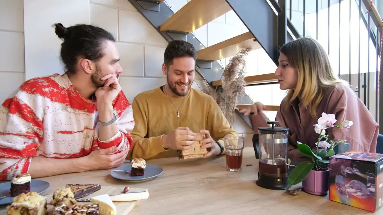Drei Personen sitzen an einem Tisch mit Kuchen und Getränken