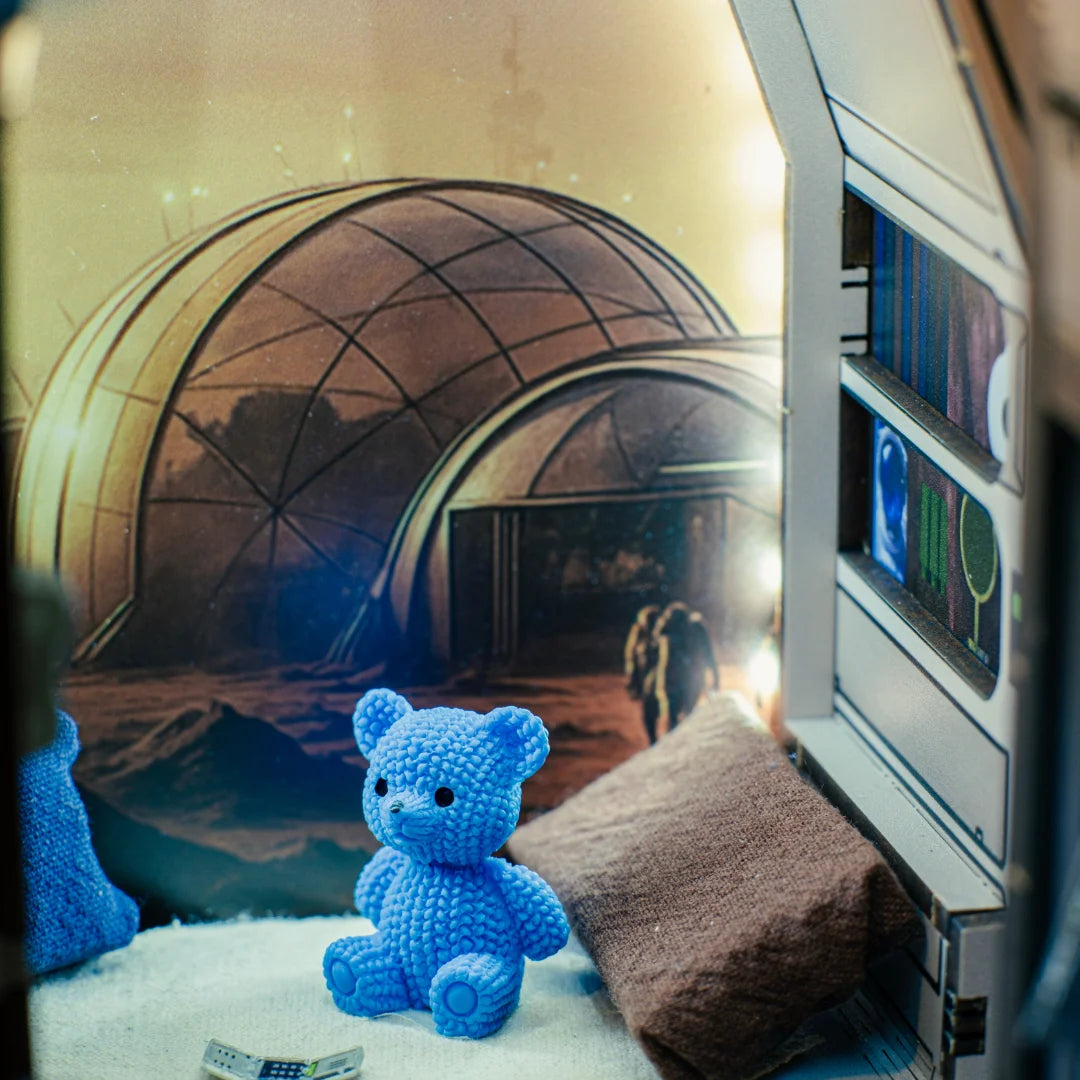 Blauer Teddybär in einer Miniaturkulisse mit Weltraumkuppel im Hintergrund