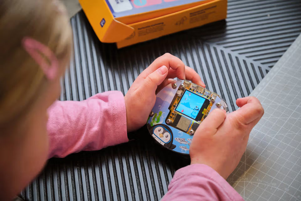 Kind hält den fertig gebauten CircuitMess Codee mit laufendem Mini-Spiel in den Händen