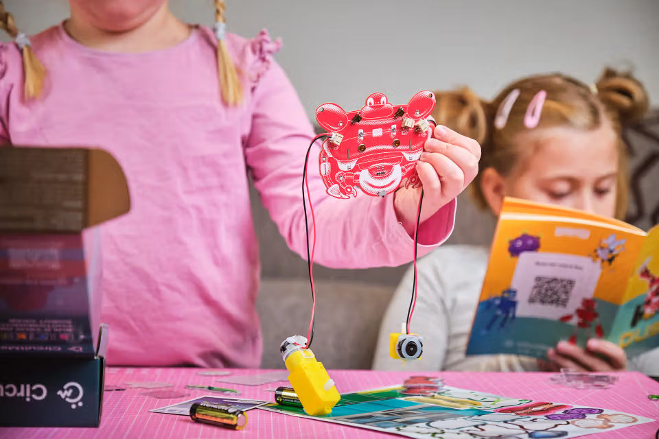 Kind hält die halbfertig zusammengebaute CircuitMess Dusty Roboterkrabbe in den Händen