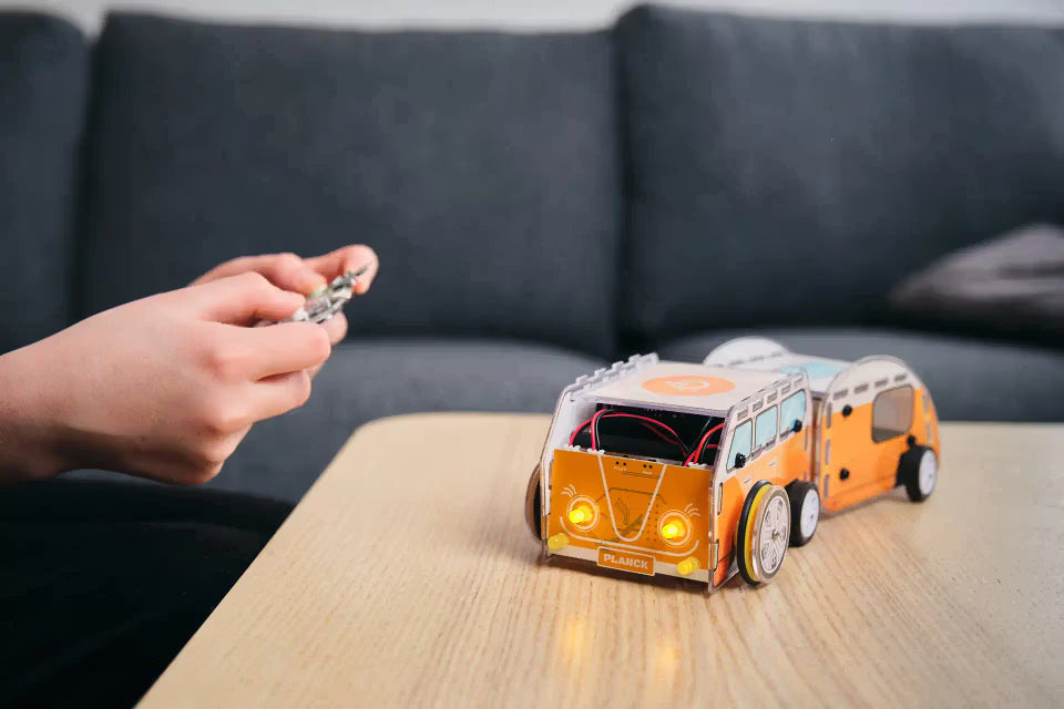 Fertig gebauter CircuitMess Planck Retro-Bulli-Roboter mit leuchtenden Scheinwerfern auf einem Tisch