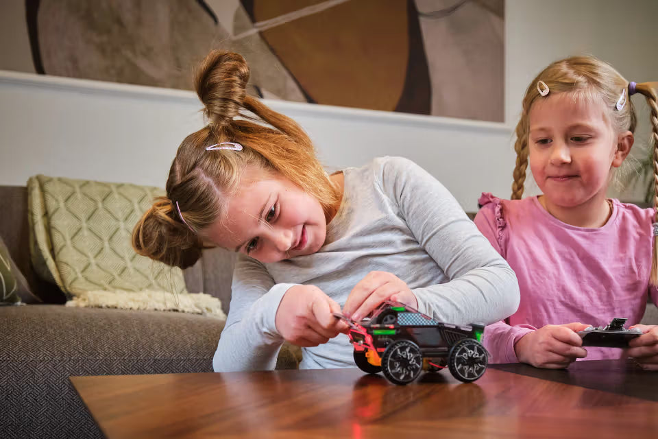 Kind baut das CircuitMess Sparkly Roboterauto zusammen, während ein weiteres Kind die Fernbedienung hält