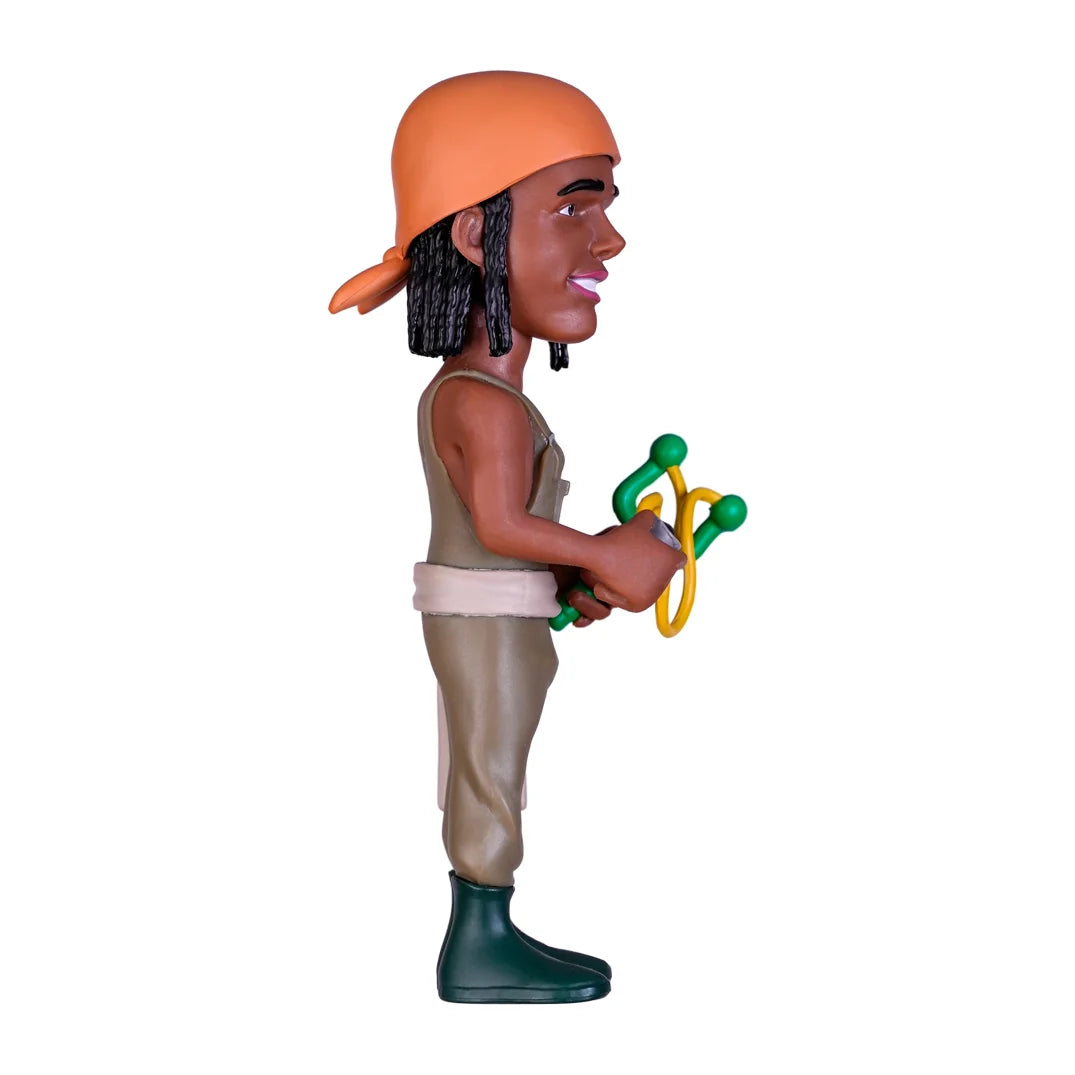 Spielfigur mit orangefarbenem Kopftuch und grüner Schleuder in der Seitenansicht